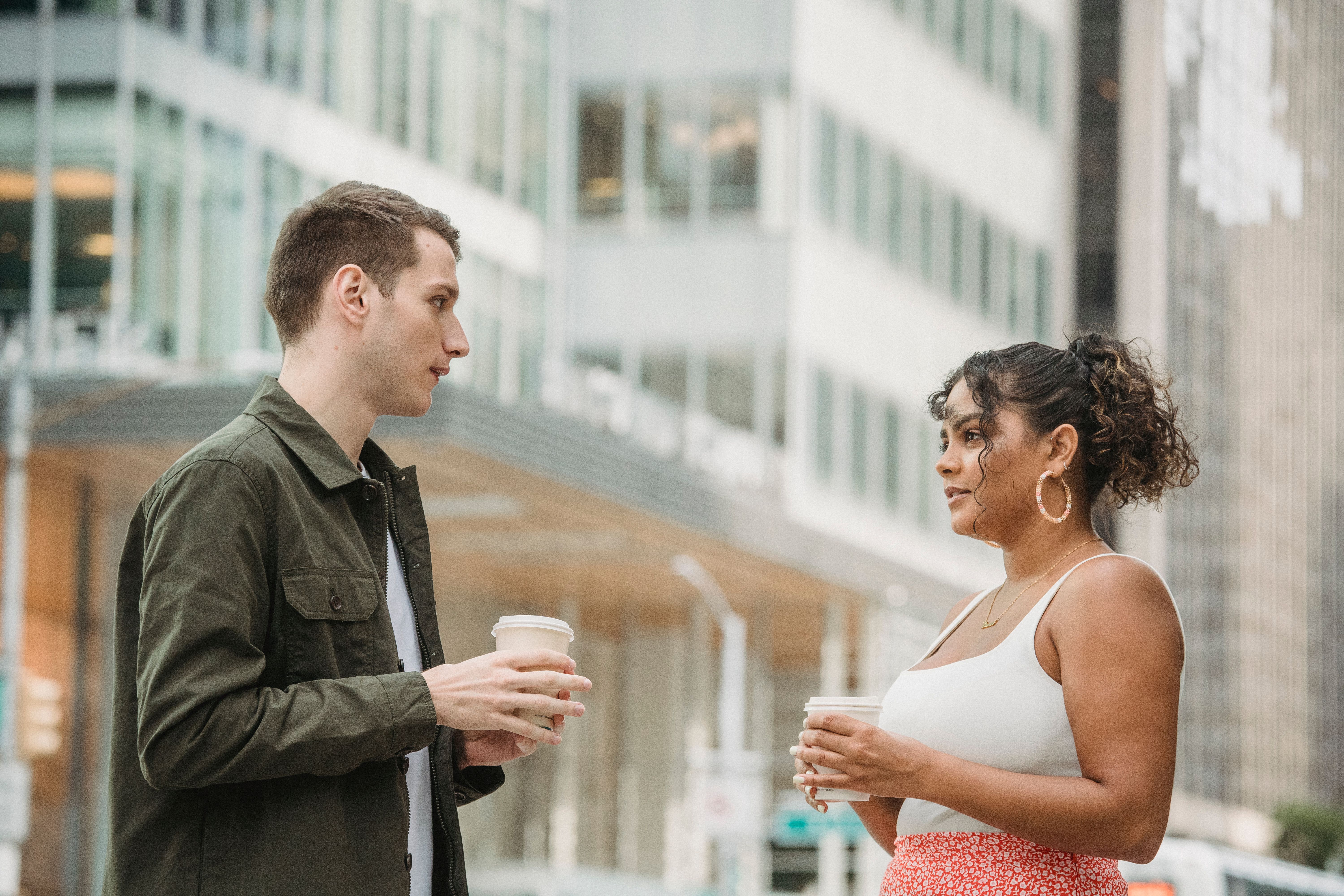 Young colleagues chatting over takeaway coffee outdoors, casual conversation among professionals