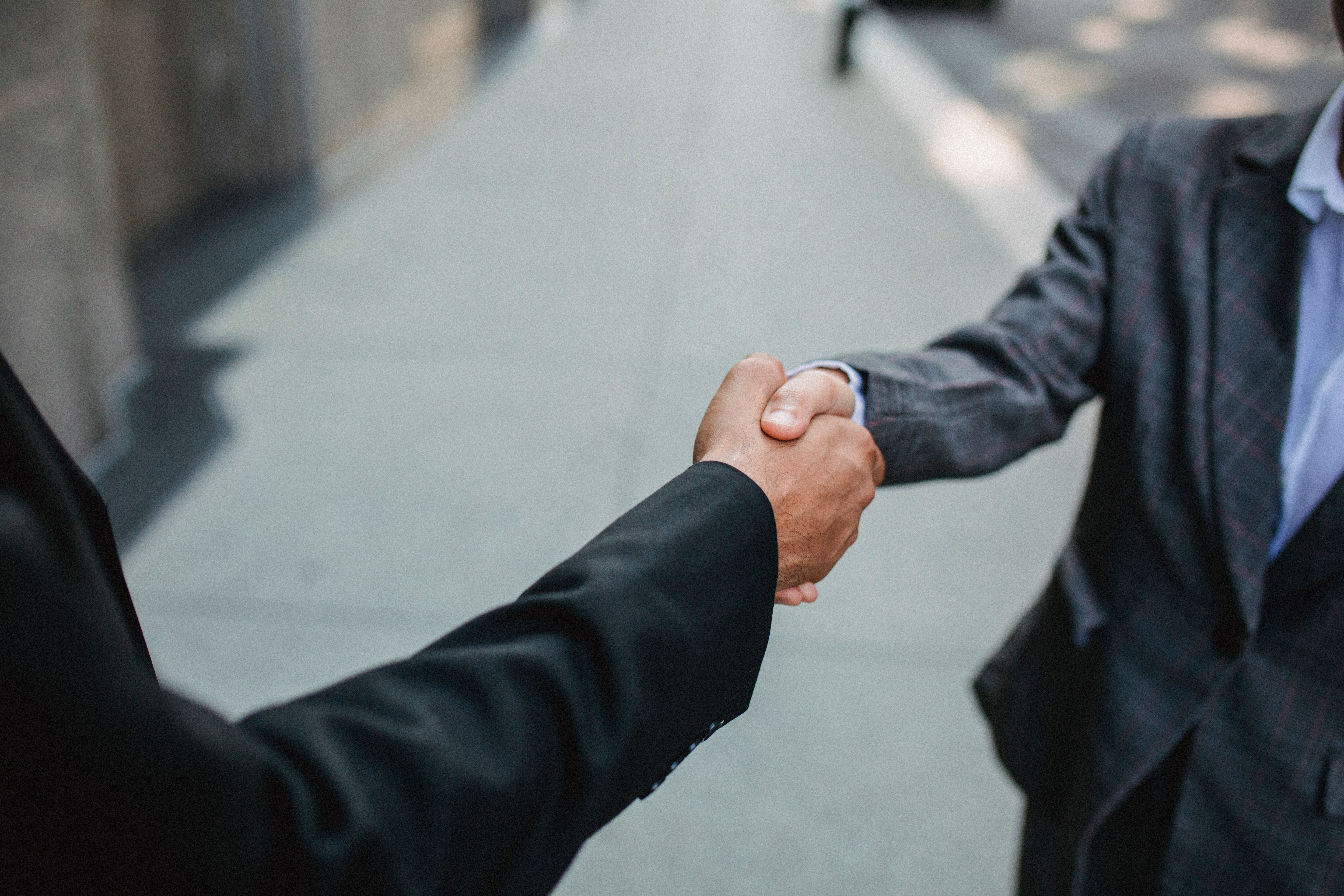 Two businessmen shaking hands outdoors, a confident first impression at a networking meeting