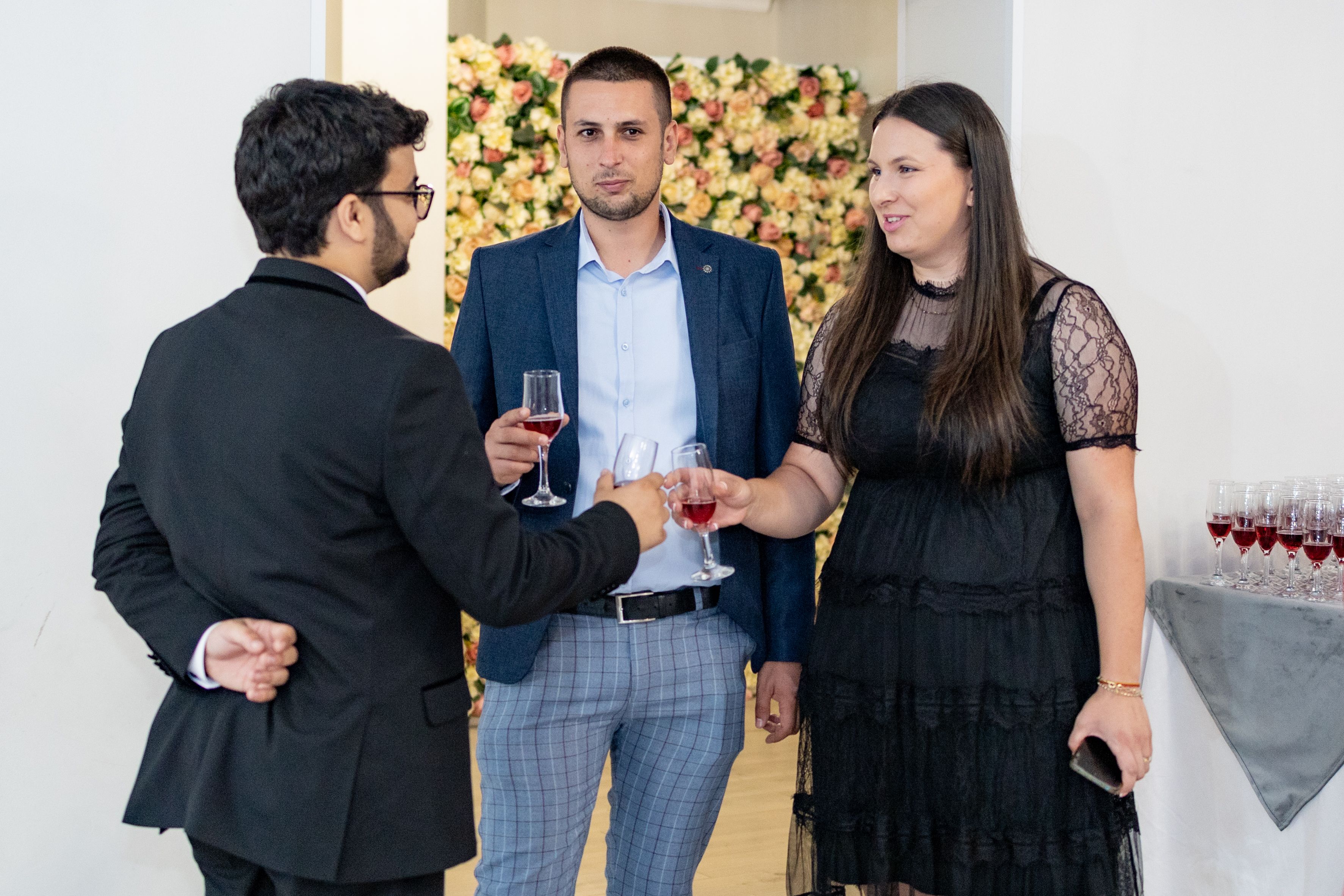 Three adults chatting and mingling with drinks at an indoor social event